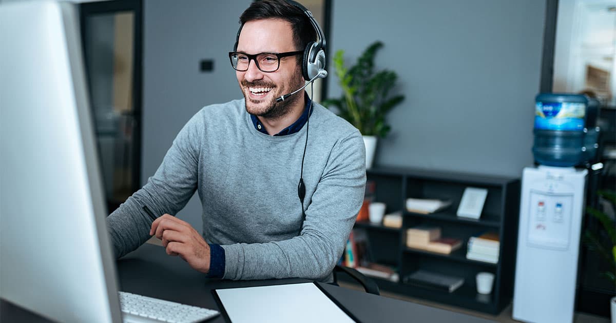 Laechelnder Mann mit Headset vor einem Computer