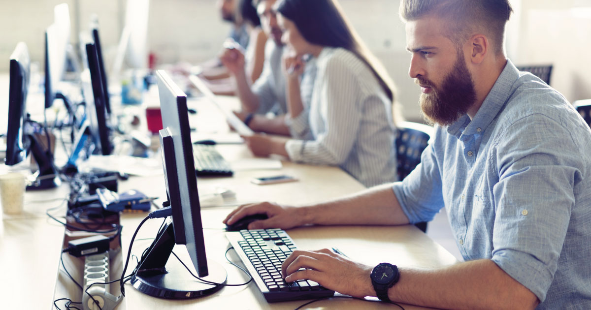 Die Kollegen konzentrieren sich auf ihre Arbeit und suchen nach Lösungen für die Probleme ihres Unternehmens, während sie an ihren Arbeitsplätzen in einer Reihe in einem hellen, modernen Büro sitzen.