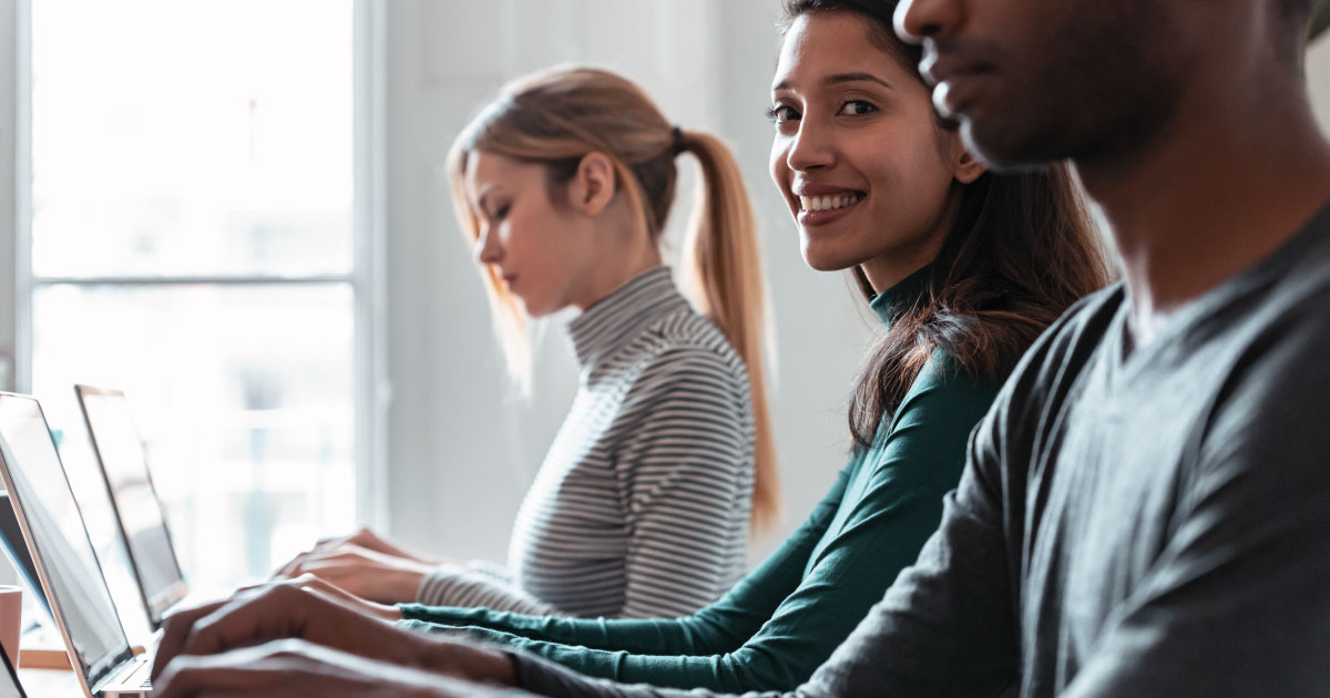 Aufnahme eines Seitenporträts einer Geschäftsfrau, die mit ihrem Laptop zwischen anderen Kollegen an einem Coworking-Platz arbeitet.